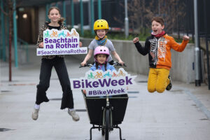 four children celebrate bikeweek 1 cycling, 1 in bike basket, 2 jumping, one with seachtain na rothar sign